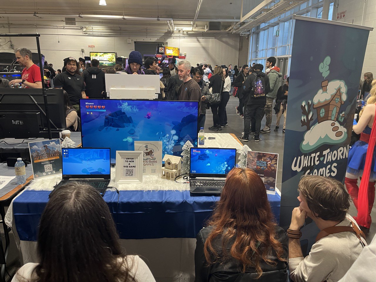 Whitethorn Games booth at a gaming expo featuring interactive gameplay videos, banners, and promotional materials with attendees engaged.